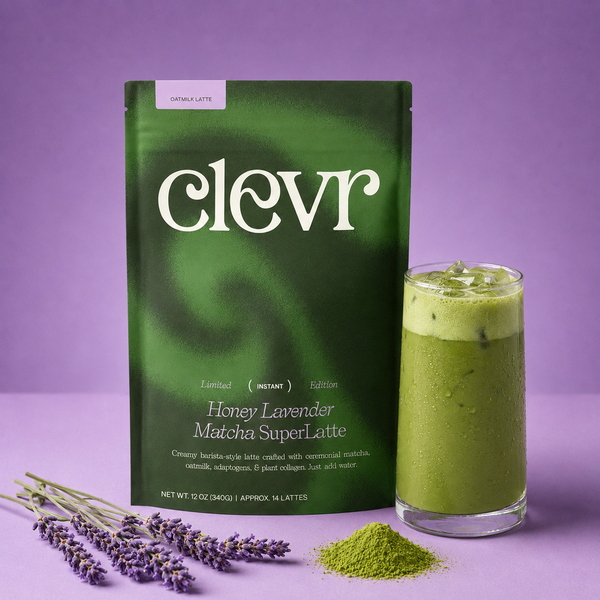 A package of Clevr Honey Lavender Matcha SuperLatte stands next to a glass of green matcha latte on a purple background, with lavender flowers and a small pile of matcha powder in front.