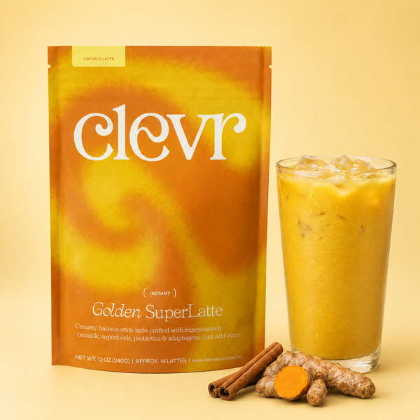 A stand-up pouch of Clevr Golden SuperLatte next to a tall glass of iced golden latte, with cinnamon sticks and a turmeric root on a warm beige background.