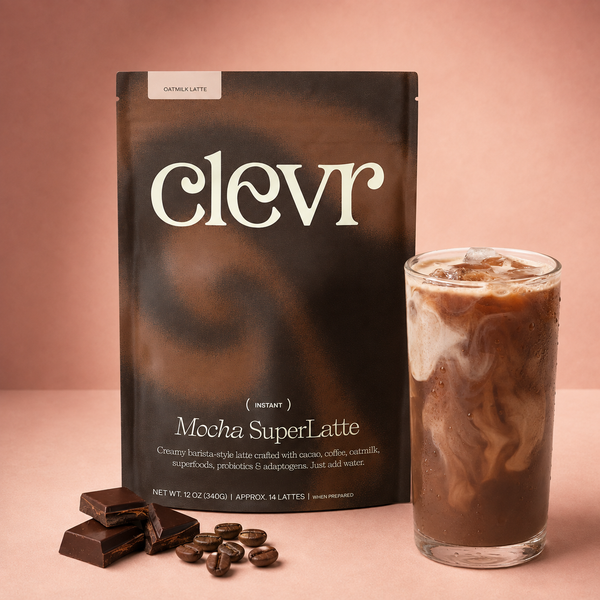 A package of Clevr Mocha SuperLatte instant coffee stands next to a glass of iced mocha latte with chocolate chunks and coffee beans on a dusty pink background.