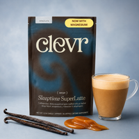 A package of clevr Sleeptime SuperLatte instant coffee lattes stands on a blue-gray background next to a glass of layered latte, vanilla beans, and caramel drizzle. The package is dark brown and black with white text and a yellow badge that says 'NOW WITH MAGNESIUM!'.